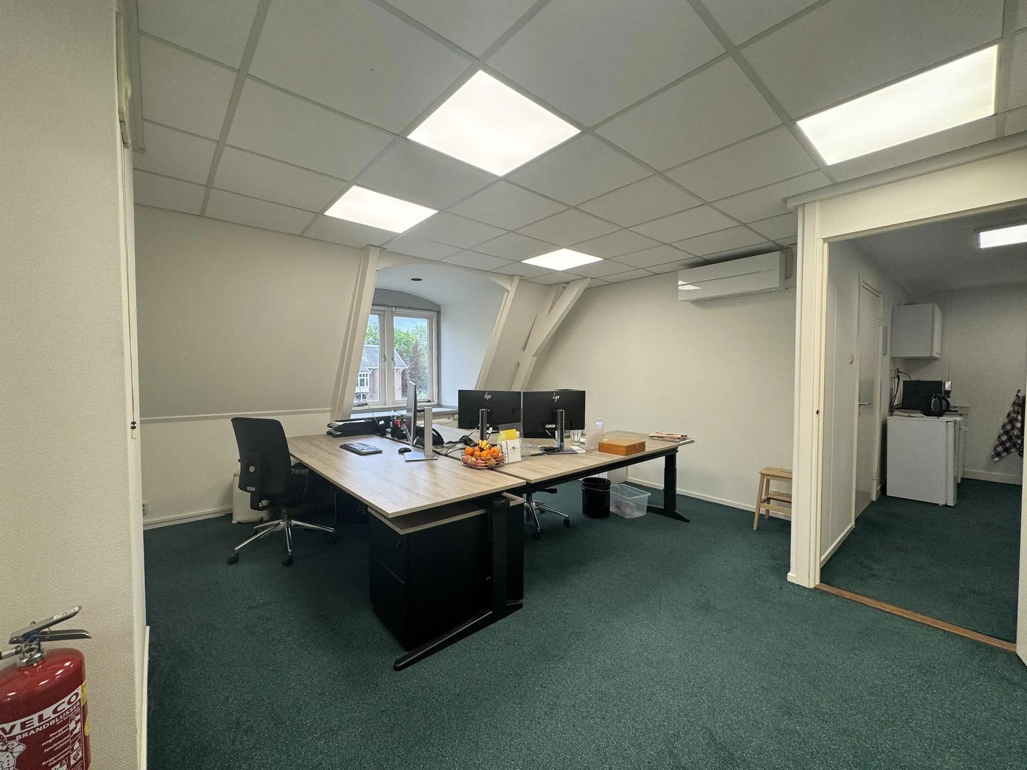 Kantoorruimte aan de Dorpsstraat met werkplekken, een raam met uitzicht en een kitchenette op de achtergrond.